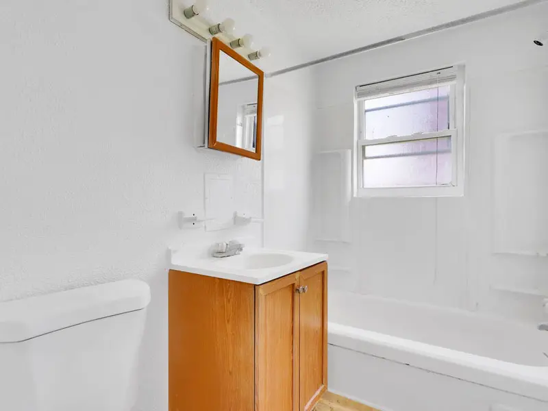 A bathroom with a shower/tub combination, window, mirror, sink, and toilet.