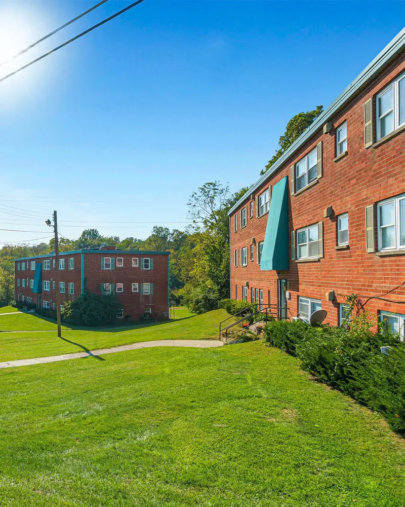 Outdoor view of 5501 @ Norwood brick 3-story apartment buildings surrounded by trees, bushes, and large areas of grass.